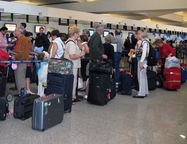 Saguão de aeroporto com vários viajantes portando os documentos para embarcar